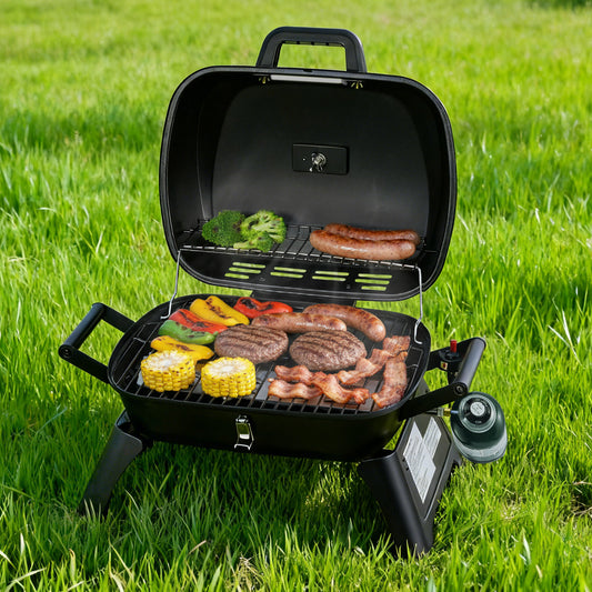 A black Royal Gourmet portable gas grill with its lid open, shown outdoors on green grass while cooking sausages, burgers, corn, and mixed vegetables.