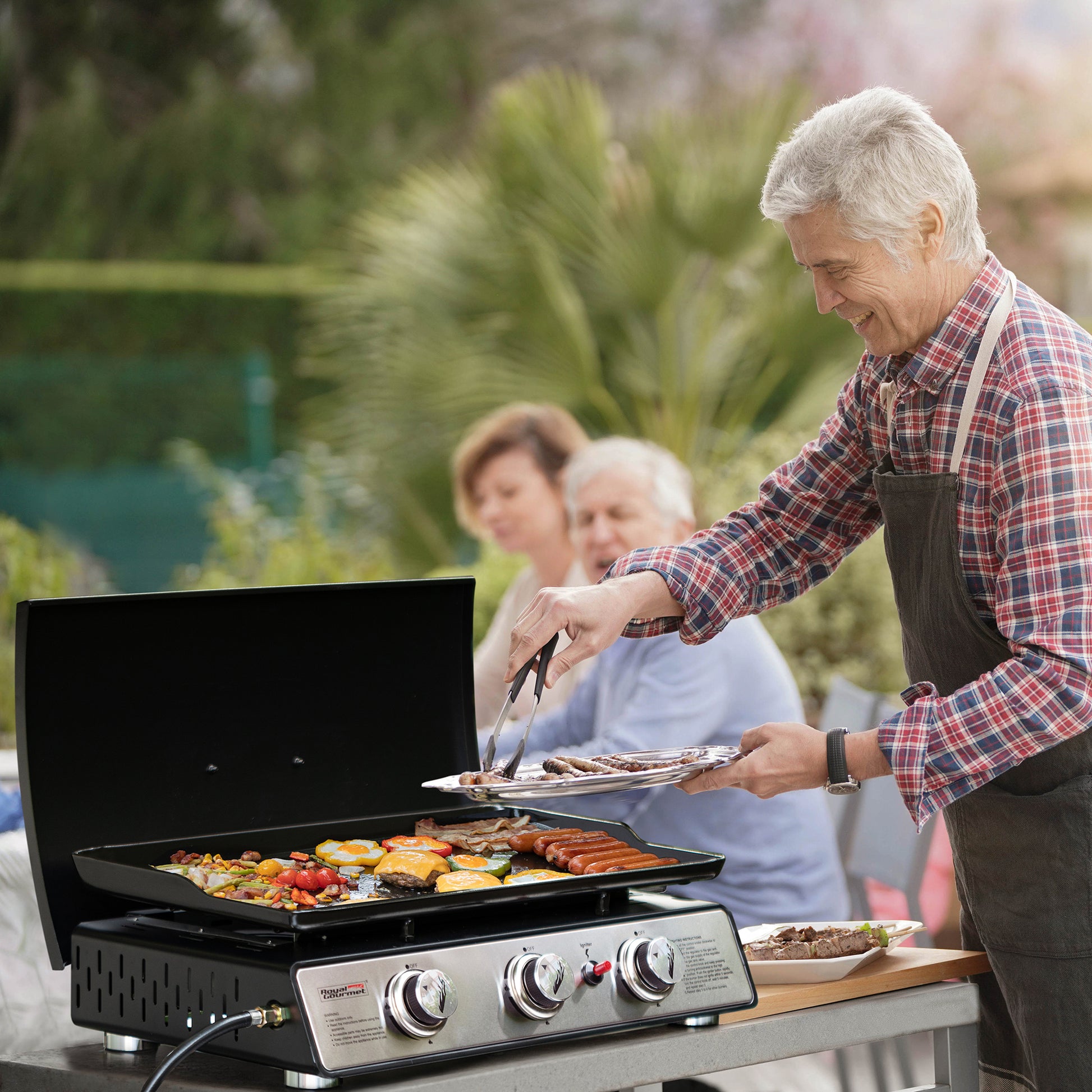 Man grilling outdoors with family in the background