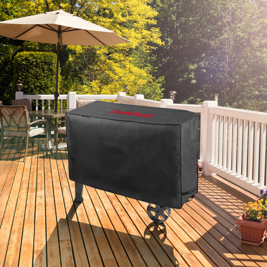 Black barbecue grill cover on a wooden deck with an umbrella and chairs in the background.