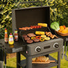 Portable Royal Gourmet grill with food and condiments on a grassy outdoor setting
