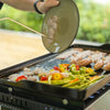 Person grilling vegetables and sausages on a Royal Gourmet portable grill outdoors.