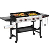 A 4-in-1 outdoor Royal Gourmet gas grill and griddle on a wheeled cart, shown with food cooking on both burners. The grill features a white control panel with red knobs, a black cart base, a paper towel holder, side tables, and hanging utensils, all isolated on a white background.
