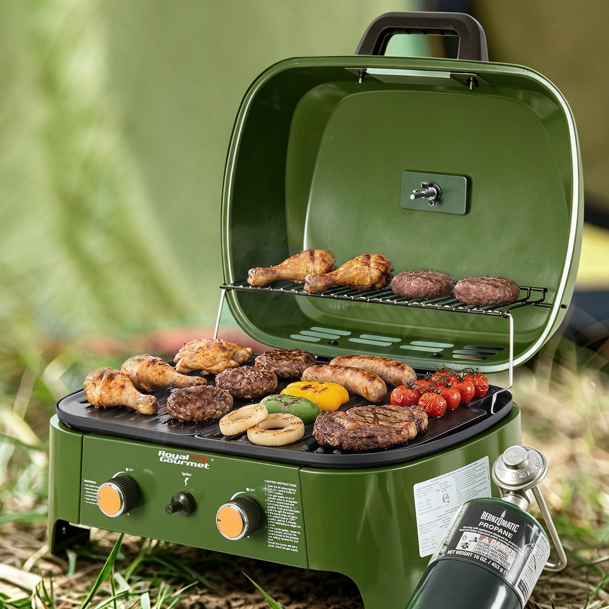 An Royal Gourmet outdoor portable camping grill in olive green, shown open with food cooking on the grates. The grill has two control knobs on the front, a carrying handle, and a propane tank attached.