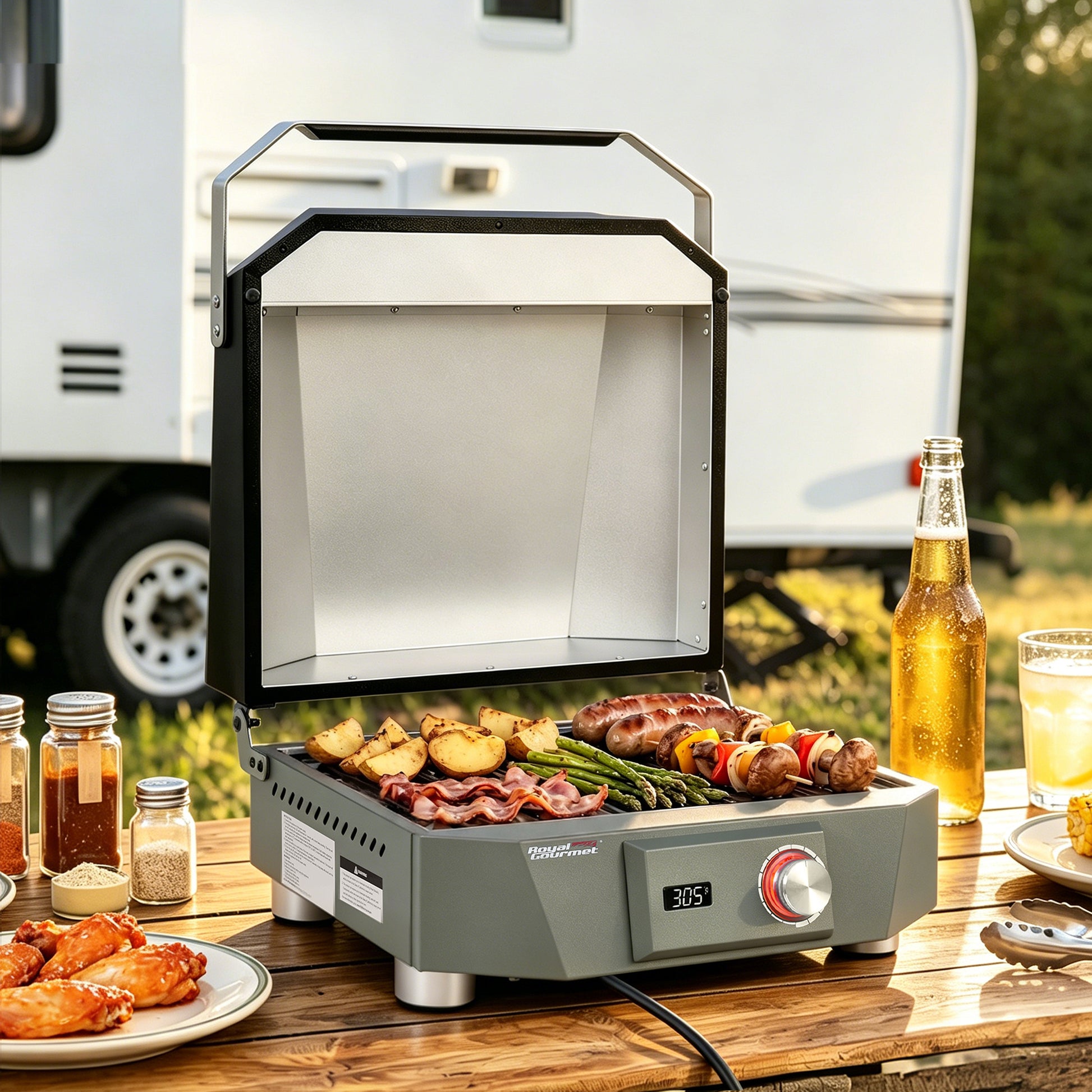 A compact electric Royal Gourmet  grill with a silver interior and gray exterior sits on a wooden picnic table outdoors, cooking skewers, bacon, potatoes, and asparagus. A bottle of beer, food plates, and a white RV are visible in the background.