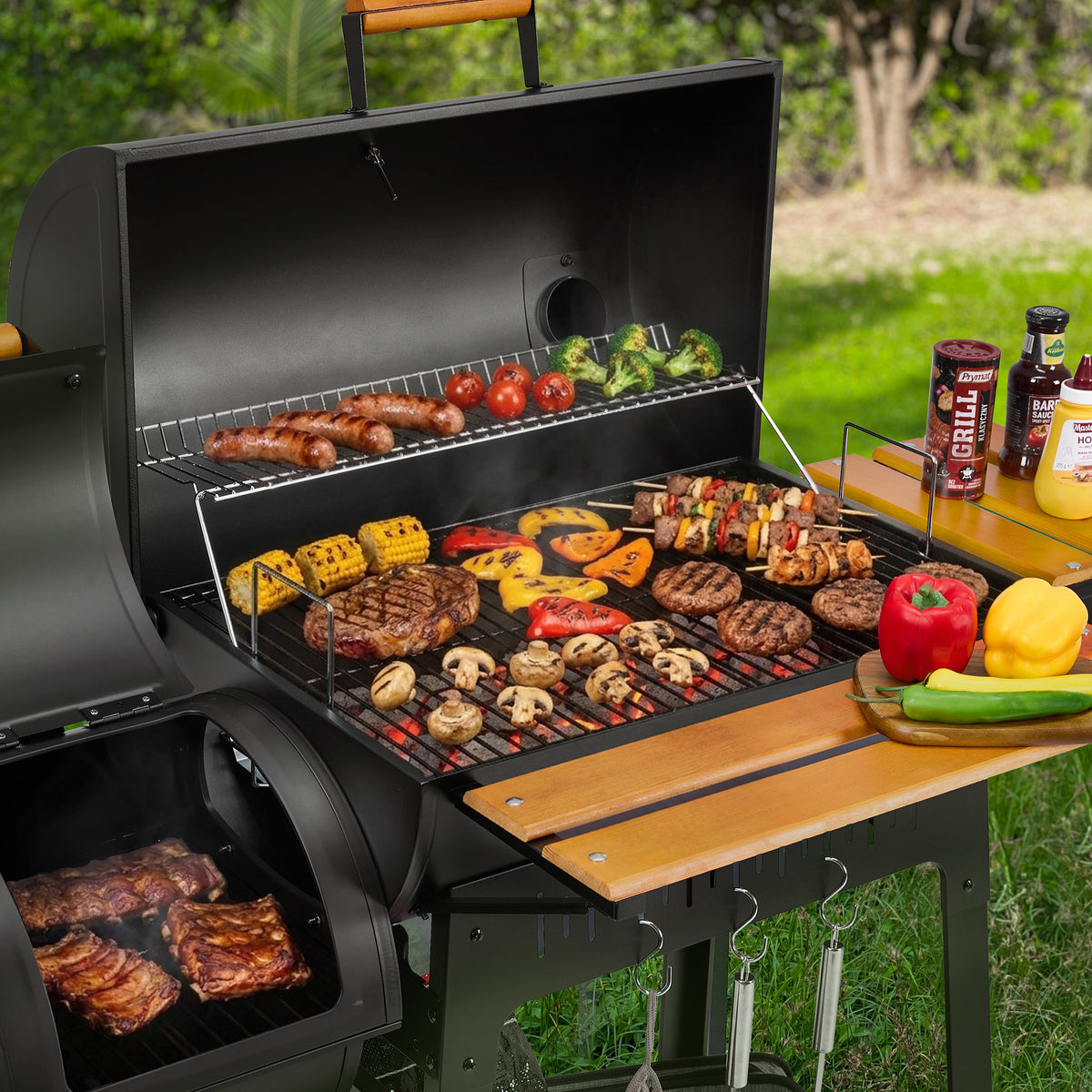 A black outdoor Royal Gourmet  gas grill with multiple food items cooking on the grates and side table, set in a grassy backyard. Condiment bottles are lined up on the side table next to fresh vegetables.