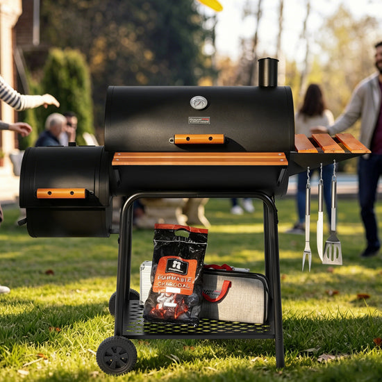 A black Royal Gourmet outdoor pellet grill with orange accents stands on a grassy lawn, with people blurred in the background and cooking accessories hanging from its side table.