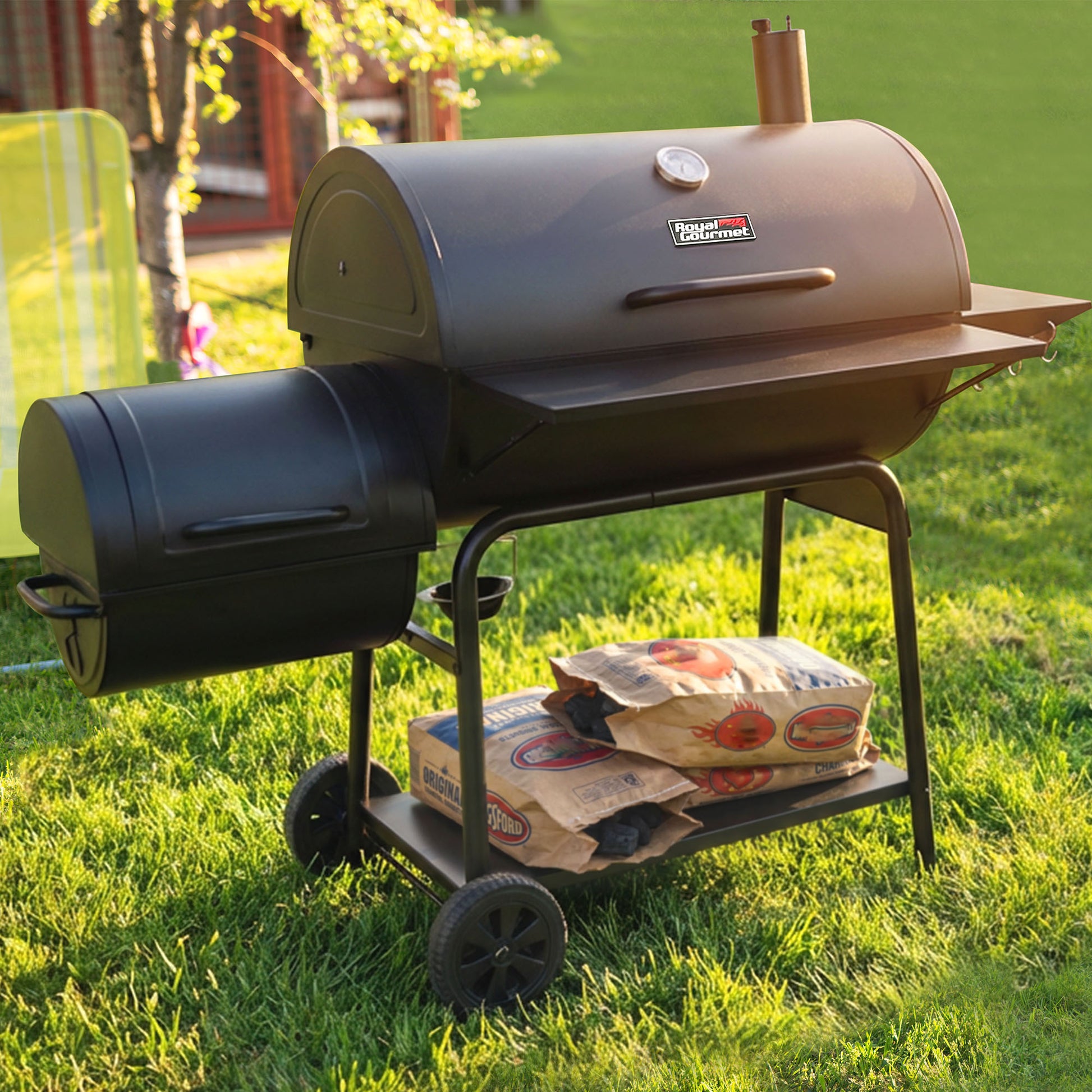 Barbecue grill on wheels with bags of charcoal in a grassy outdoor setting