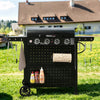 A black outdoor Royal Gourmet grill cart with side tables, hanging utensils, a paper towel holder, and a lower shelf with condiment bottles, photographed on a grassy lawn in front of a house.