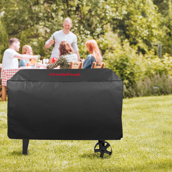 Black grill cover with 'Crescent' branding on a grassy outdoor setting with people in the background.