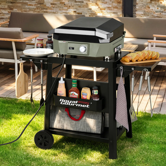 A black outdoor Royal Gourmet gas grill on a matching rolling cart, set on a grassy patio with food items and condiments displayed on and around it.