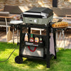 A black outdoor Royal Gourmet gas grill on a matching rolling cart, set on a grassy patio with food items and condiments displayed on and around it.