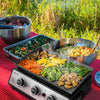 Outdoor cooking setup with a portable Royal Gourmet grill, vegetables, and pasta on a red checkered tablecloth.