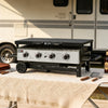 Portable outdoor Royal Gourmet grill on a table with a beer and utensils, set against an RV background.