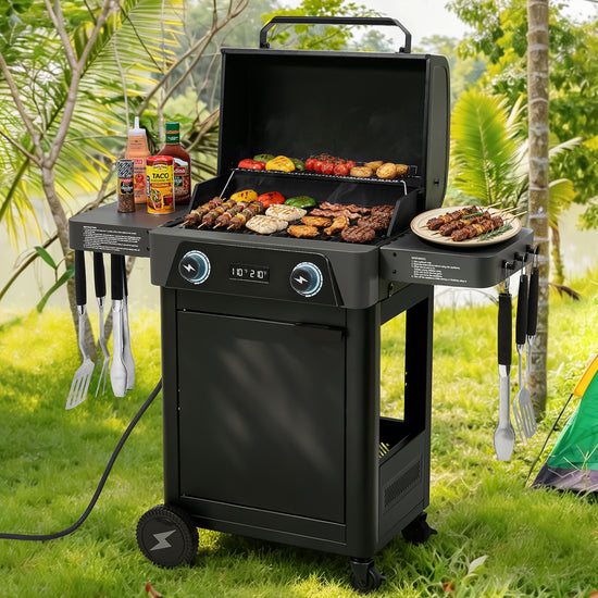 A black outdoor Royal Gourmet electric grill with a lid, shown open and cooking meat and vegetables on the grates. The grill has side tables holding bottles, utensils, and a plate of food, and is set on grass in a garden-like outdoor environment with trees and a tent in the background.