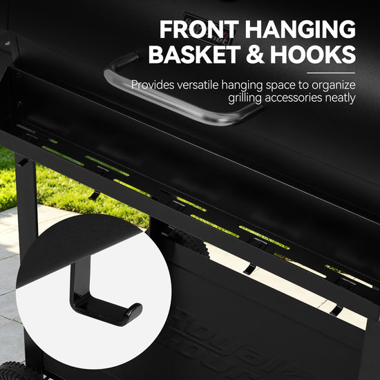 Close-up of a black Royal Gourmet grill with text reading 'FRONT HANGING BASKET & HOOKS' and a circular inset showing the hook detail. A small outdoor area with grass and pavement is visible in the background.