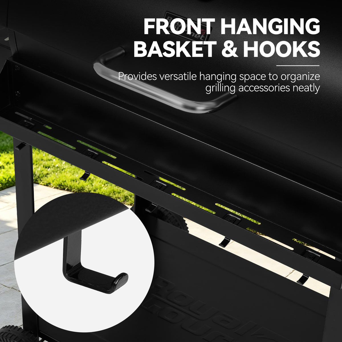 Close-up of a black Royal Gourmet grill with text reading 'FRONT HANGING BASKET & HOOKS' and a circular inset showing the hook detail. A small outdoor area with grass and pavement is visible in the background.
