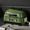 An outdoor Royal Gourmet propane grill in olive green with two orange control knobs, shown inside a car trunk.