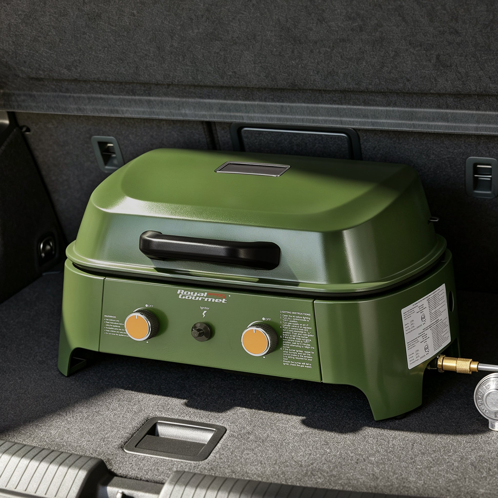 An outdoor Royal Gourmet propane grill in olive green with two orange control knobs, shown inside a car trunk.