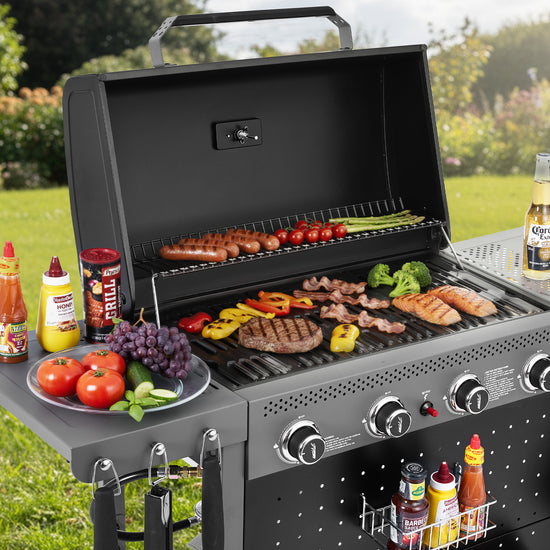 Gas grill with food and condiments on a grassy outdoor setting