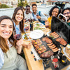 Group of people enjoying a barbecue outdoors with a Royal Gourmet portable grill.