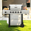 A Royal Gourmet gas grill with side shelves, set on a green lawn in front of a patio. The grill is white and black with five control knobs on the front, a propane tank connected underneath, and food and condiments on its side tables.