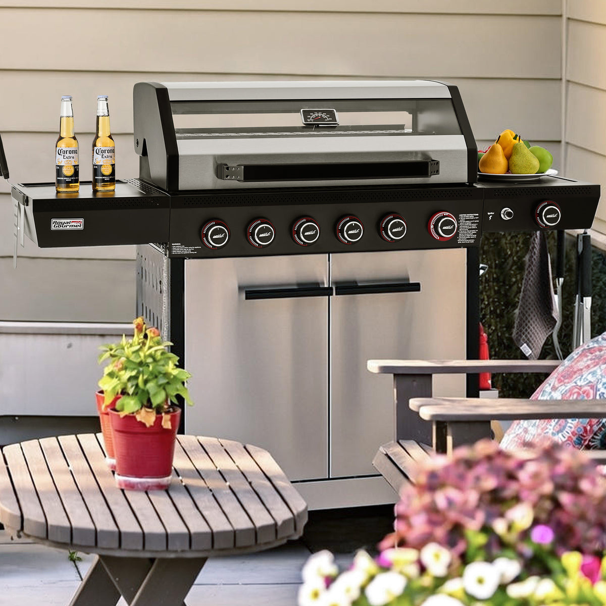 A stainless steel and black Royal Gourmet outdoor gas grill with side tables and beer bottles on a patio, with a potted plant in the foreground.