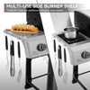 A split-view product image showing a stainless steel side burner Royal Gourmet grill shelf setup. The left panel shows the open side shelf holding sliced bread on a wooden board and hanging utensils, with text at the top reading 'MULTI-USE SIDE BURNER SHELF' and '12,000 BTU heat with additional workspace when needed.