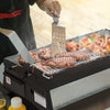 Person grilling meat and vegetables on a Royal Gourmet  portable grill with a visible brand logo.