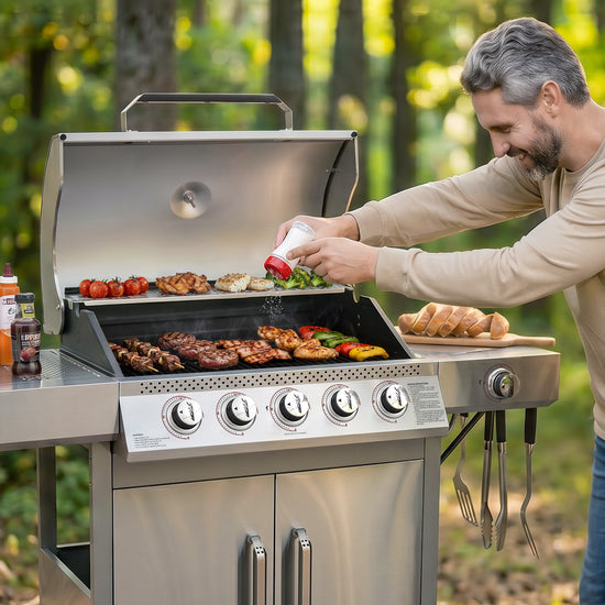 A man grilling outdoors on a stainless steel Royal Gourmet gas barbecue grill with food cooking on the grates and side shelf, set against a blurred forest background.