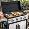 A stainless steel Royal Gourmet outdoor gas grill with the lid open, cooking sausages, eggs, asparagus, and cheese on a flat top griddle. The grill is shown outdoors on a stone patio with food props and condiments nearby.