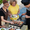 Three people grilling outdoors with a focus on food preparation.