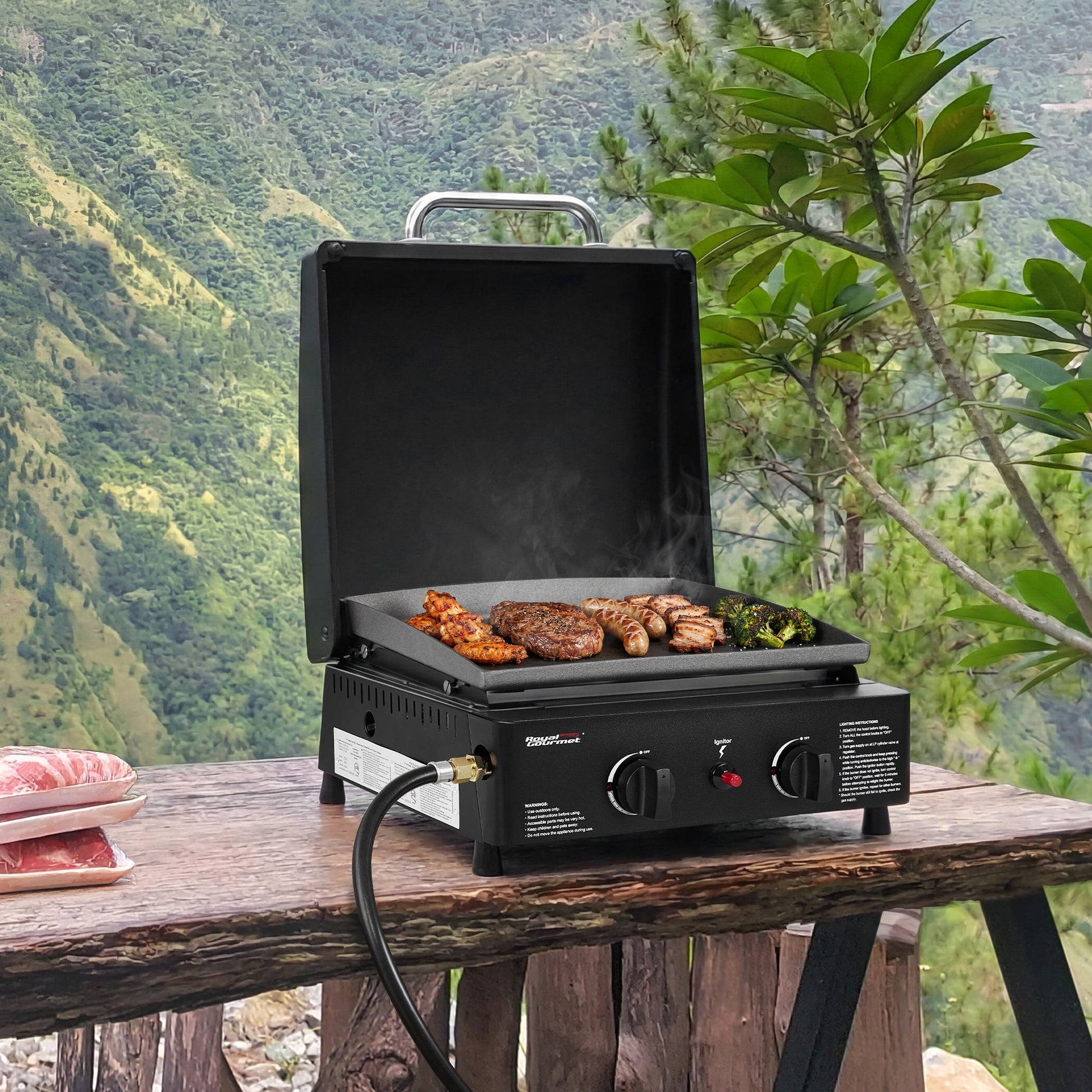 Royal Gourmet Portable grill with food on a wooden table outdoors with a mountainous background