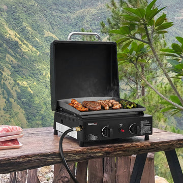 Royal Gourmet Portable grill with food on a wooden table outdoors with a mountainous background