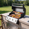 An outdoor Royal Gourmet  gas grill with a stainless steel and black body, shown open and cooking various foods on a built-in wooden deck grill cabinet in a backyard setting.