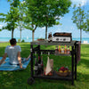 Person sitting on a blanket by a Royal Gourmet grill cart with food and drinks outdoors.