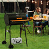 Royal Gourmet Black barbecue grill on a grassy outdoor area with people sitting at a table in the background.