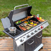 A stainless steel Royal Gourmet gas grill with the lid open, shown outdoors on a wooden deck with grass in the background. The grill is loaded with cooked meats, vegetables, skewers, and a pot on the side burner, with condiments placed on top.