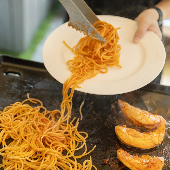 Noodles being transferred from a plate to a pan with prawns.