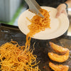 Noodles being transferred from a plate to a pan with prawns.