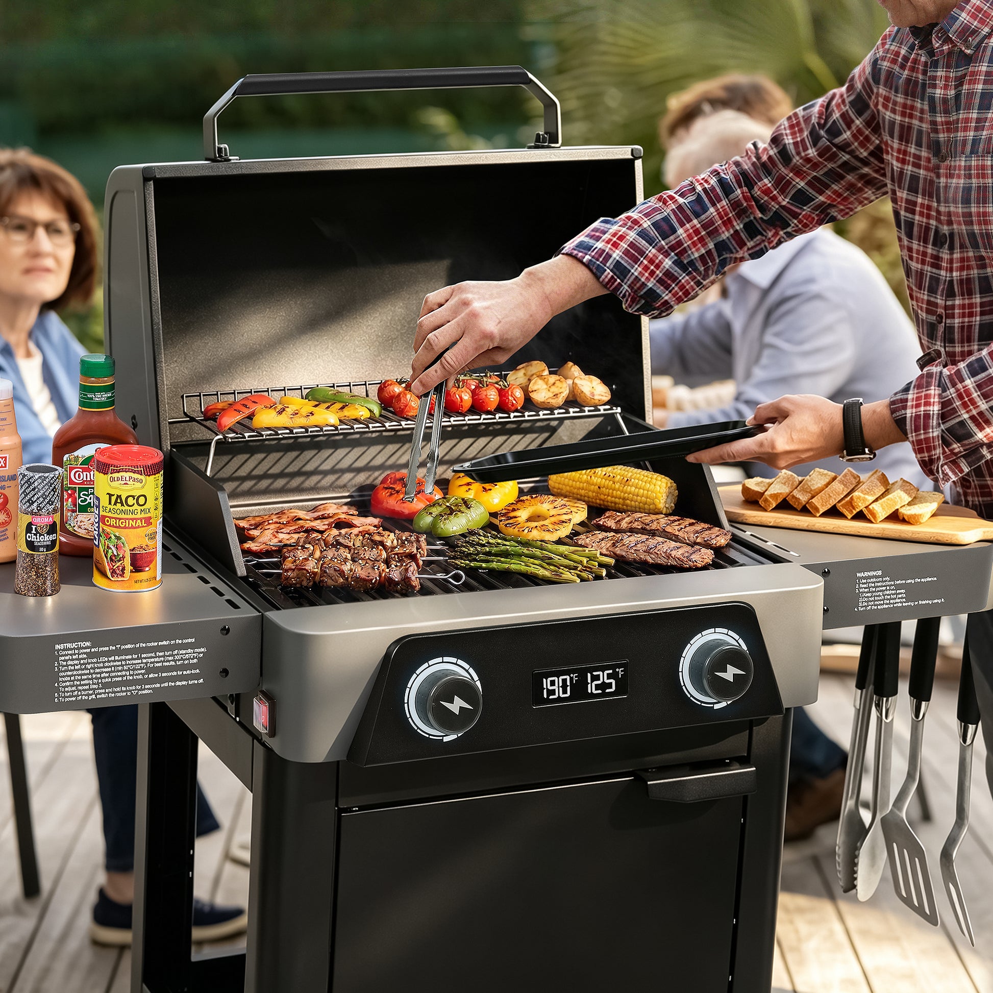 A black and stainless steel outdoor Royal Gourmet gas grill is shown on a wooden deck with food cooking inside, including steak, peppers, corn, and mushrooms. A person in a plaid shirt is tending the grill, with other people blurred in the background.