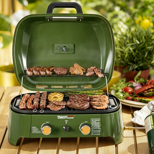 An olive green portable Royal Gourmet gas grill with food cooking inside, set on a wooden table with a blurred garden and outdoor dining background.