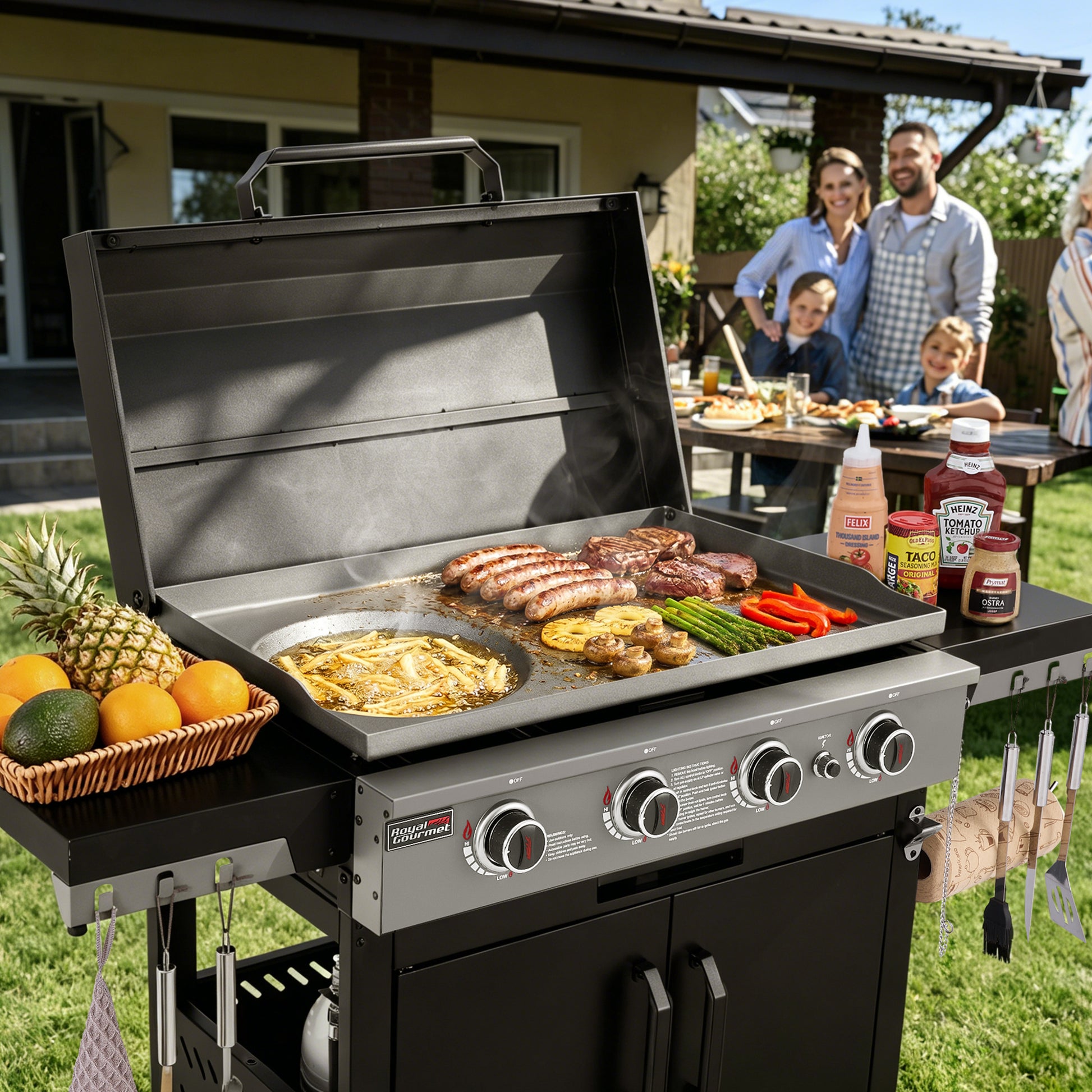 A black and stainless steel outdoor Royal Gourmet  gas grill is shown open in a backyard setting, cooking sausages, steaks, burgers, asparagus, and vegetables. A basket of fruit sits on the side table, and a family is visible dining in the background.