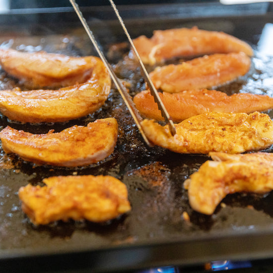 Sliced peaches being grilled on a hot surface with skewers.