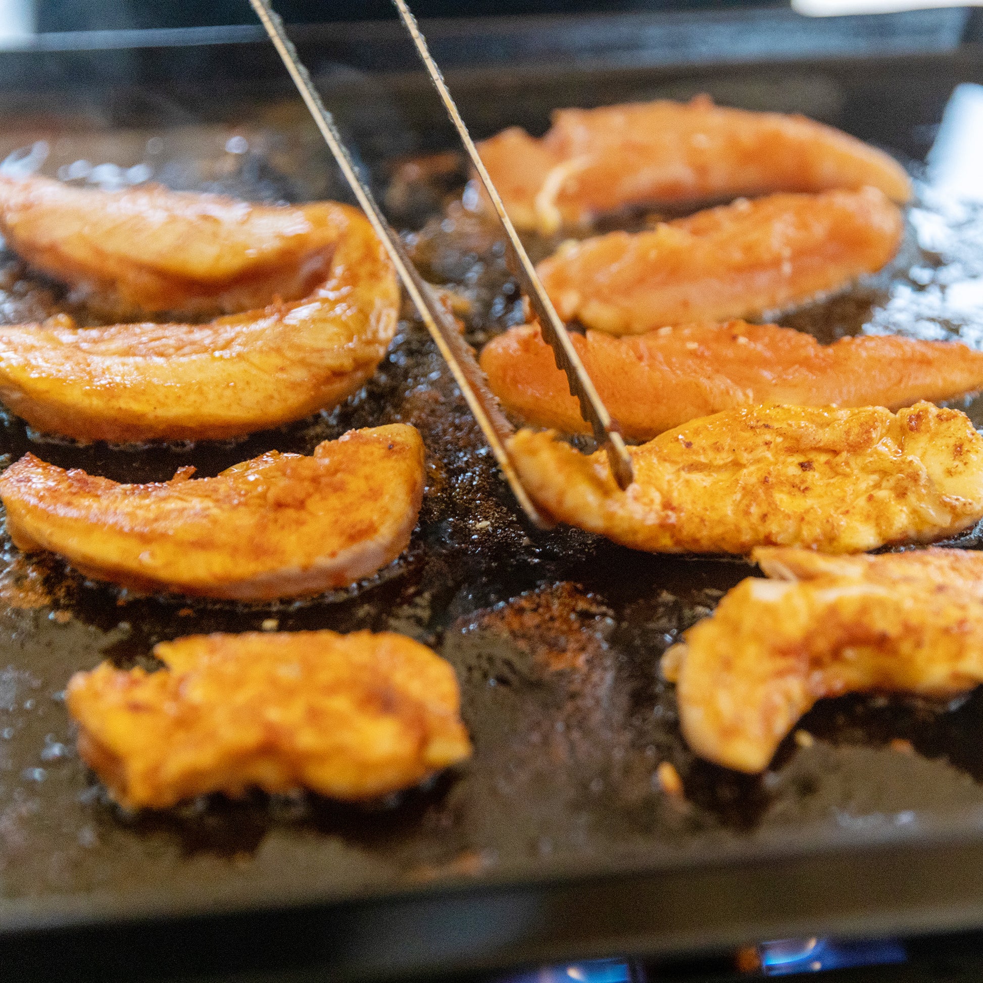 Sliced peaches being grilled on a hot surface with skewers.