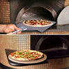 Collage of a pizza being placed in an oven and the finished product on a stone surface.