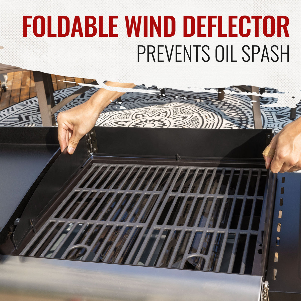 A close-up of a black foldable wind deflector installed on the side of a grill, with a person's hands holding the panel in place. The text overlay at the top reads 'FOLDABLE WIND DEFLECTOR PREVENTS OIL SPASH'.