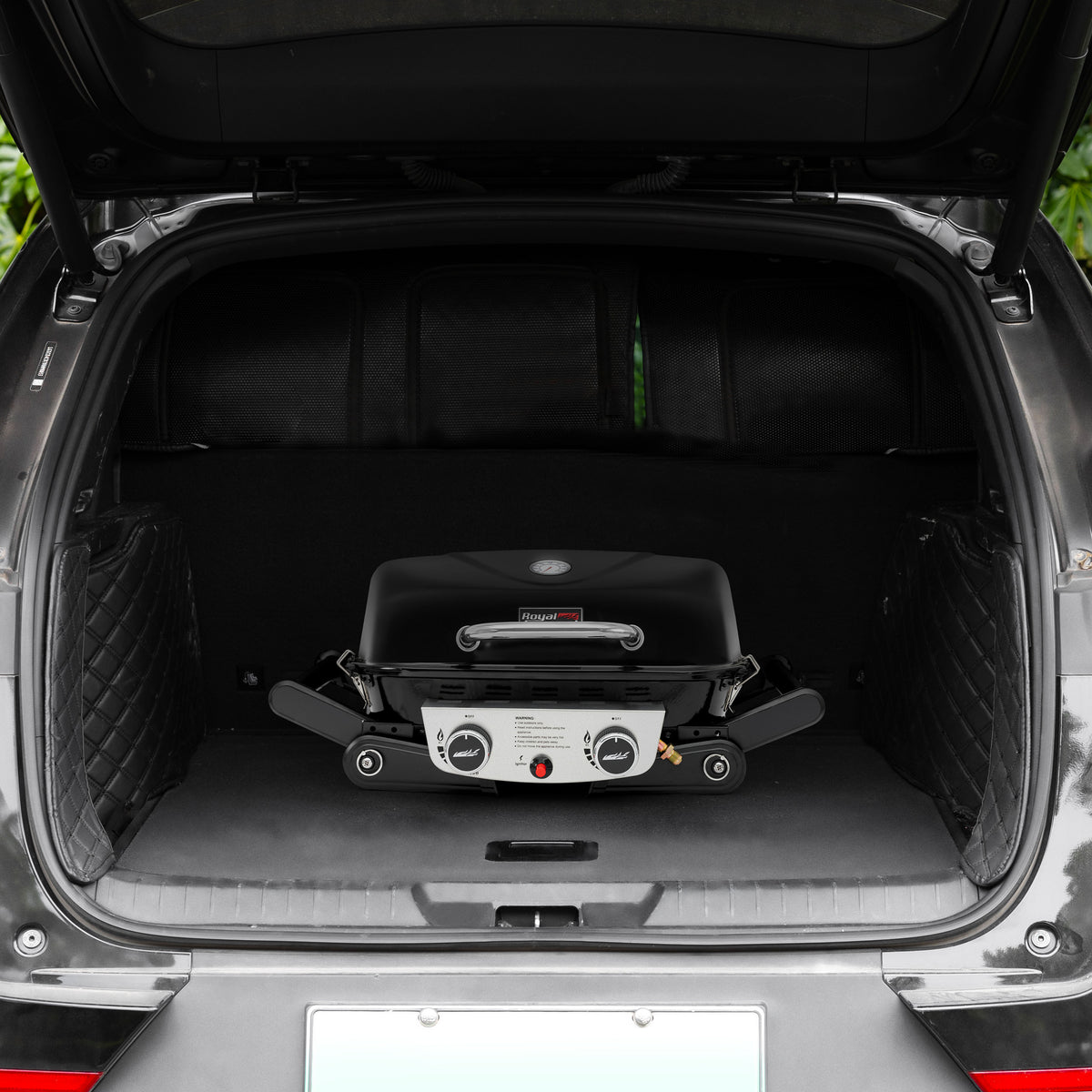 A compact black Royal Gourmet gas grill with a silver control panel is folded and displayed inside the open trunk of a black vehicle.