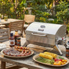 Stainless steel Royal Gourmet  grill on a wooden table with food and condiments outdoors