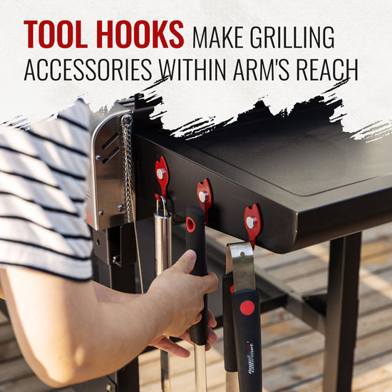 A person's hand hangs a tool from a black grill's side-mounted hook, with other tools stored on the hook. Large text at the top reads 'TOOL HOOKS MAKE GRILLING ACCESSORIES WITHIN ARM'S REACH'.