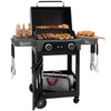 A black 3-in-1 Royal Gourmet gas grill cart with an open lid, loaded with food on the grates and side tables, shown on a white background. The cart includes side tables holding bottles and utensils, a lower storage shelf with a bag, and control knobs on the front.